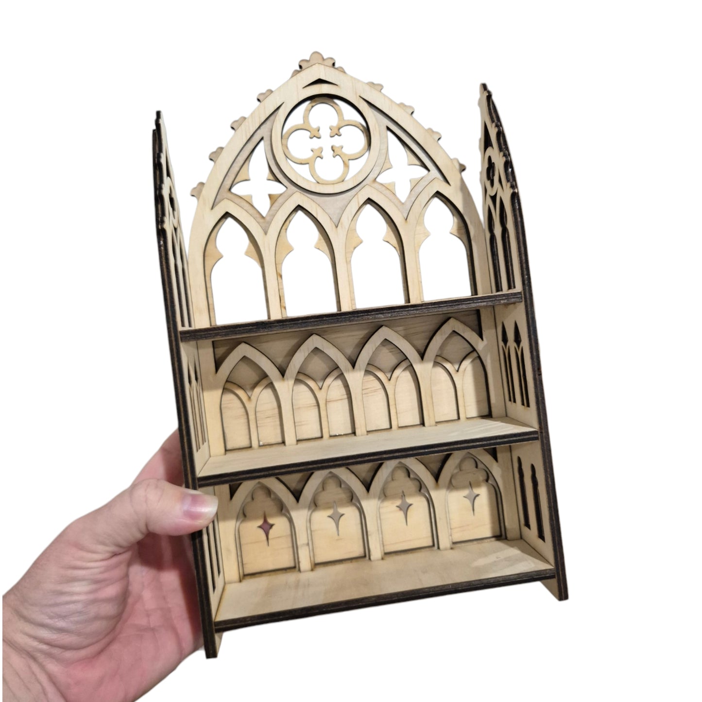 A hand holding a small wooden gothic-style shelf or organizer with laser-cut arched panels and two tiers, shown against a plain white background.